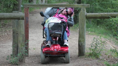 Frau mit Rollstuhl fährt unter niedrigem Klettergerüst durch